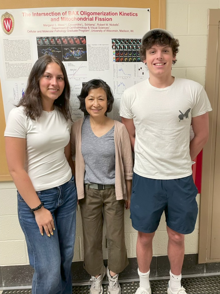 Three smiling lab members stand in front of a research poster