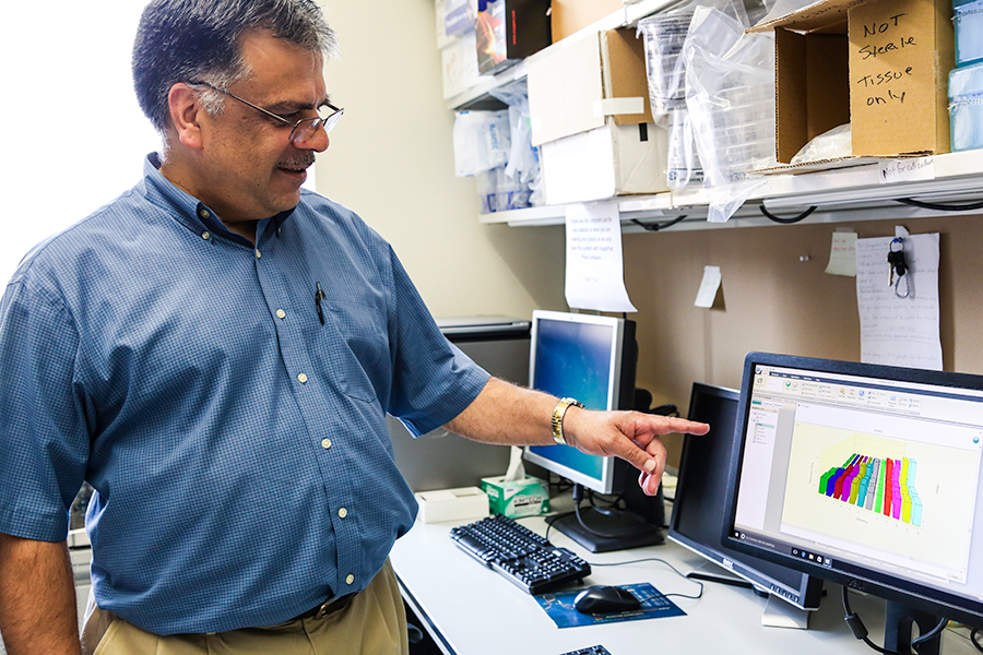A man in a blue shirt points to a computer monitor.